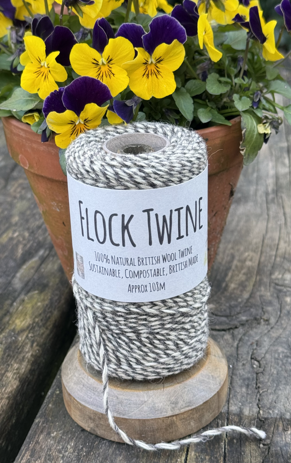 Image of a spool of flock twine in the garden with a pot of pansies